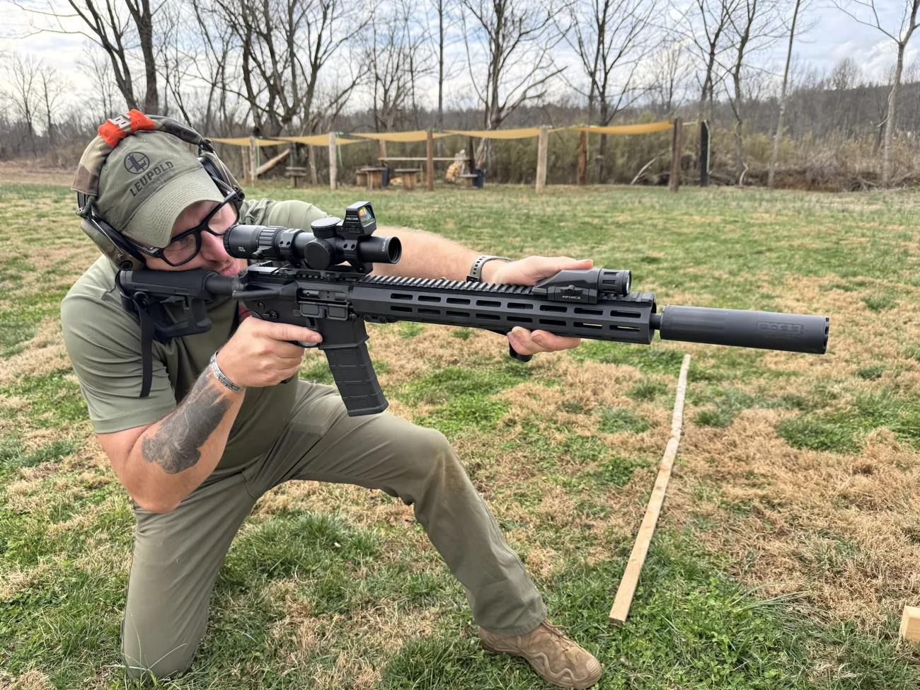 A shooter kneeling and firing a suppressed carbine during live-fire training
