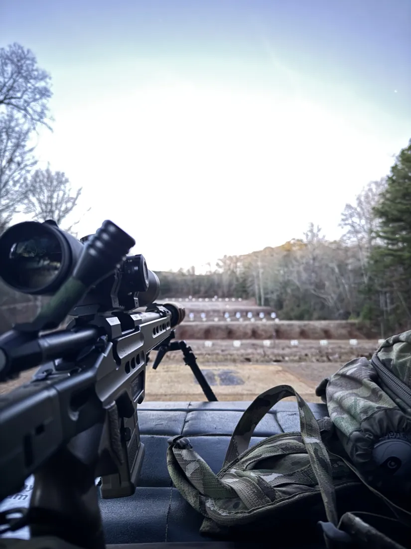 A scoped precision rifle resting on a bench at dusk